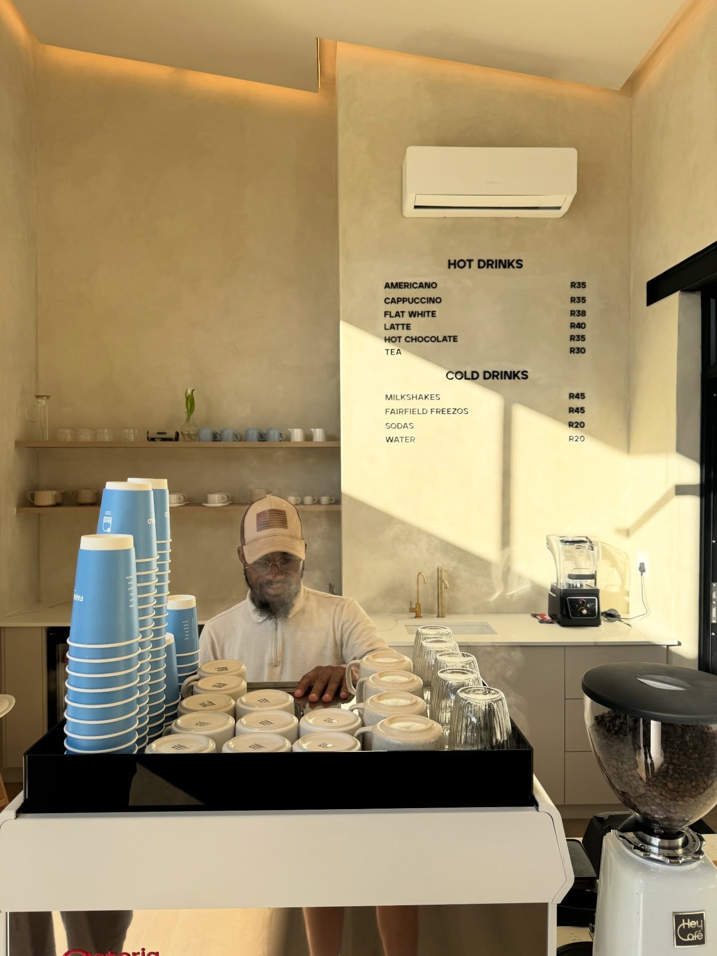 Barista behind the counter at Fairfield Coffee with the menu board and branded cups